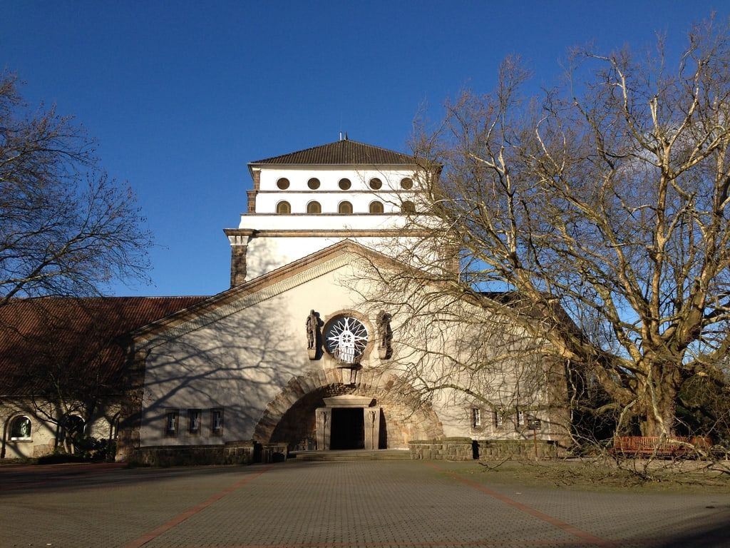 Frontansicht des expressionistischen Hauptgebäudes mit breitem Rundbogenportal, strahlenförmig gegliedertem Rundfenster und gestuftem Turm unter kahlen Bäumen auf Hauptfriedhof Dortmund